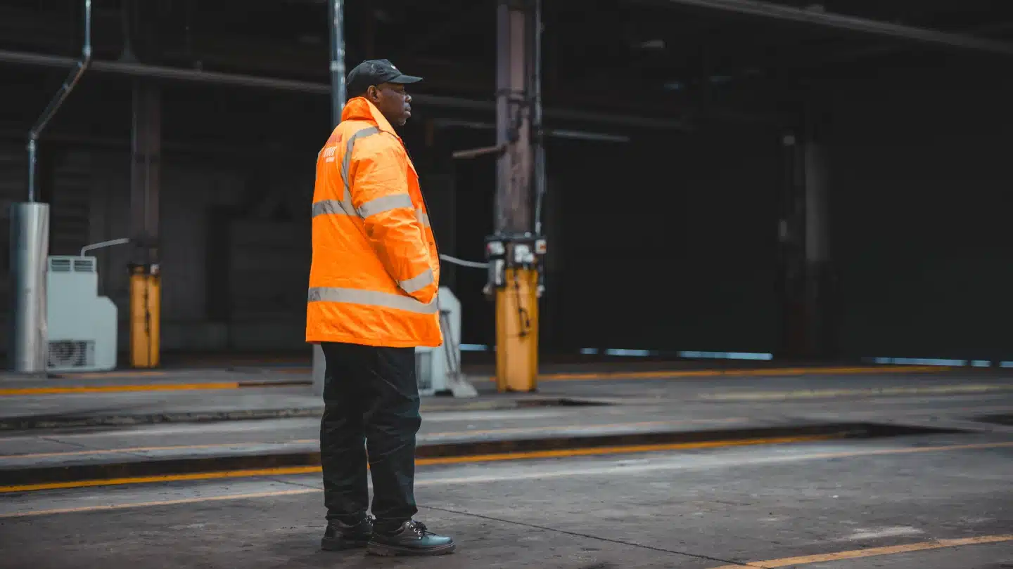 A uniformed manned security officer in a high-visibility jacket standing in a large industrial space