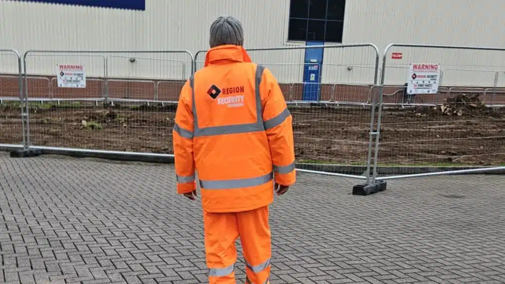 SIA licensed security for a utility site in Sheffield with a guard in an orange high-vis suit facing a fenced area