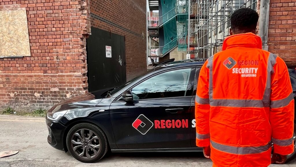 A security guard stands next to a Region Security Guarding patrol car on a site, representing our Stafford security company.