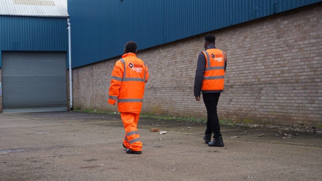 Two Region Security Guarding personnel in orange high-visibility jackets, patrolling a warehouse site, representing security guards Stoke-on-Trent