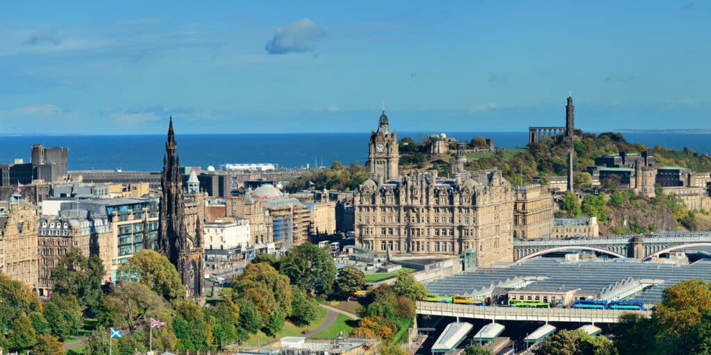 Panoramic view of a historic city with ornate buildings, a large railway station, and the sea in the background.
