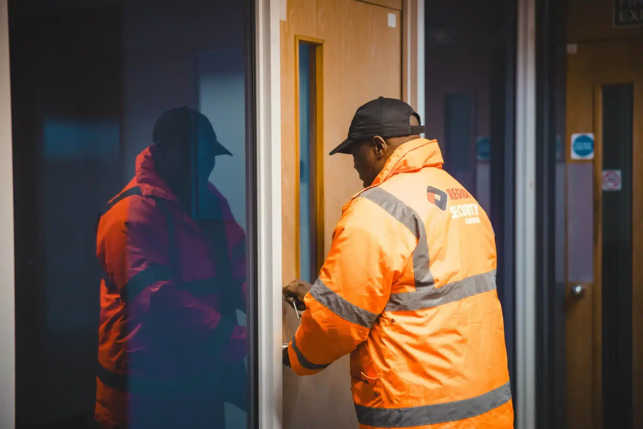Security guard in a high-visibility jacket unlocking a door inside a building.
